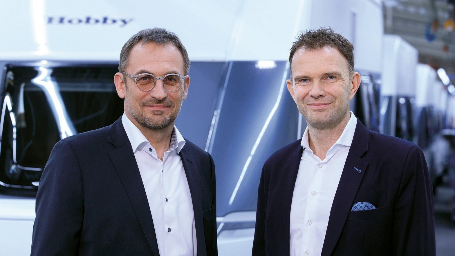 Die Geschäftsführer stehen vor einem neu produzierten Hobby Wohnwagen und blicken freundlich lächelnd in die Kamera